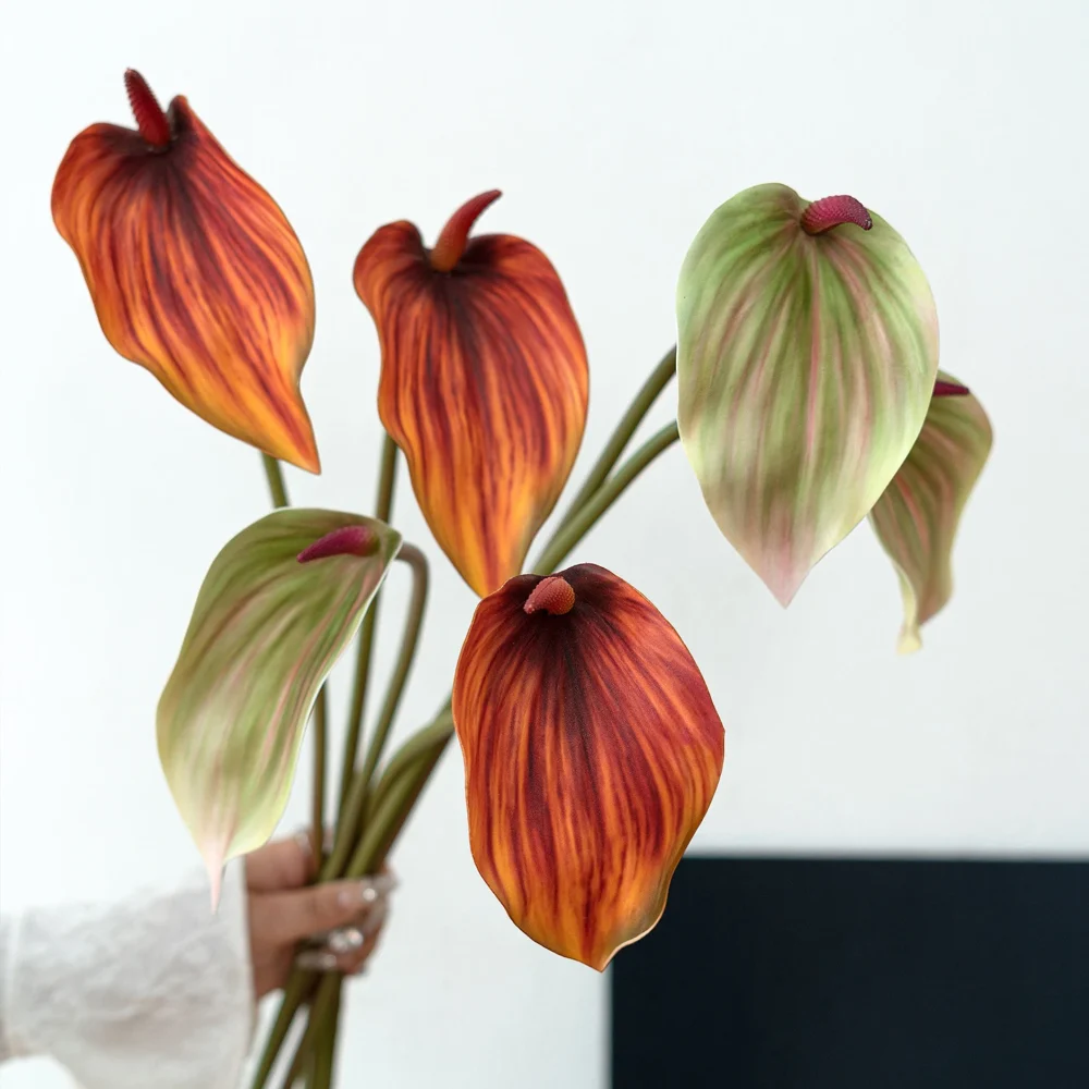 Orange and green artificial anthurium stem with one glossy spathe and an upright spadix, held in one hand