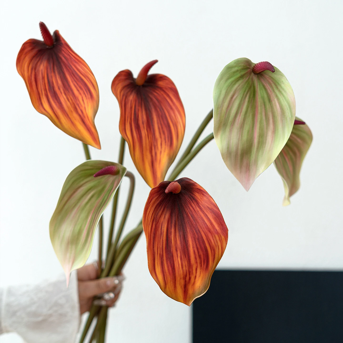 Orange and green artificial anthurium stem with one glossy spathe and an upright spadix, held in one hand