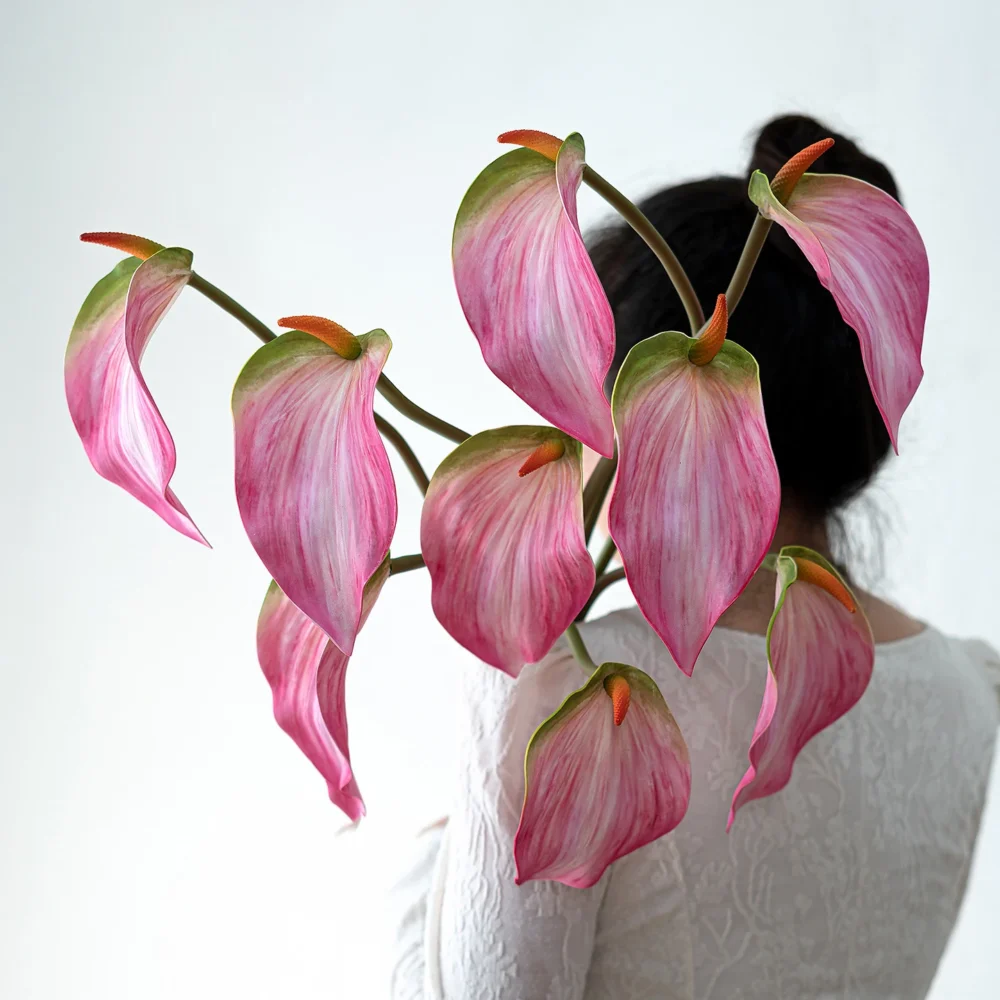 Pink artificial anthurium stem with one glossy spathe and an upright spadix, held in one hand