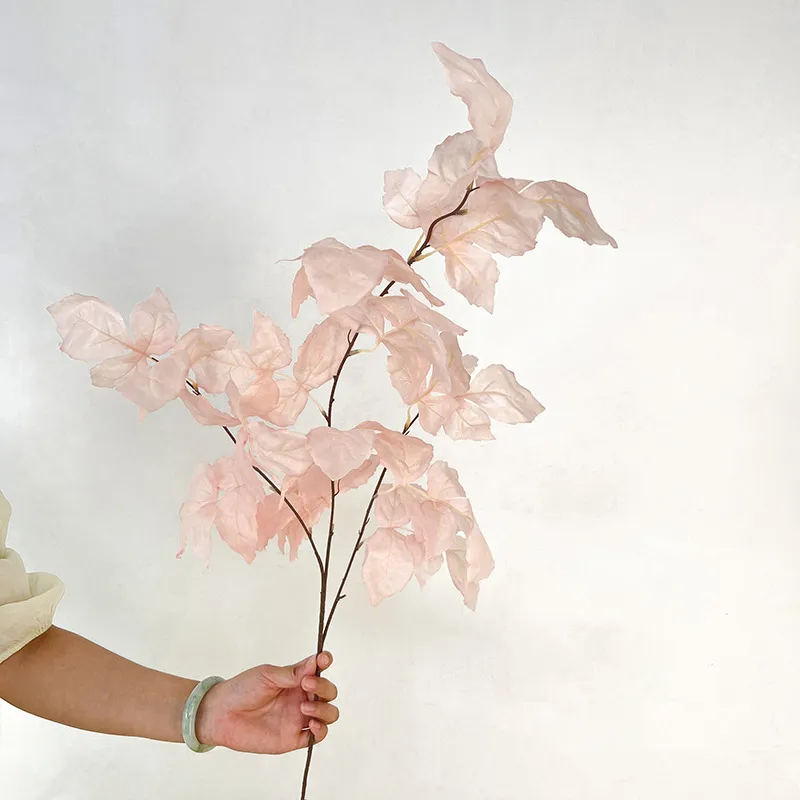 Blush artificial autumn leaf stem of small oval leaves on a fine woody branch, held in one hand