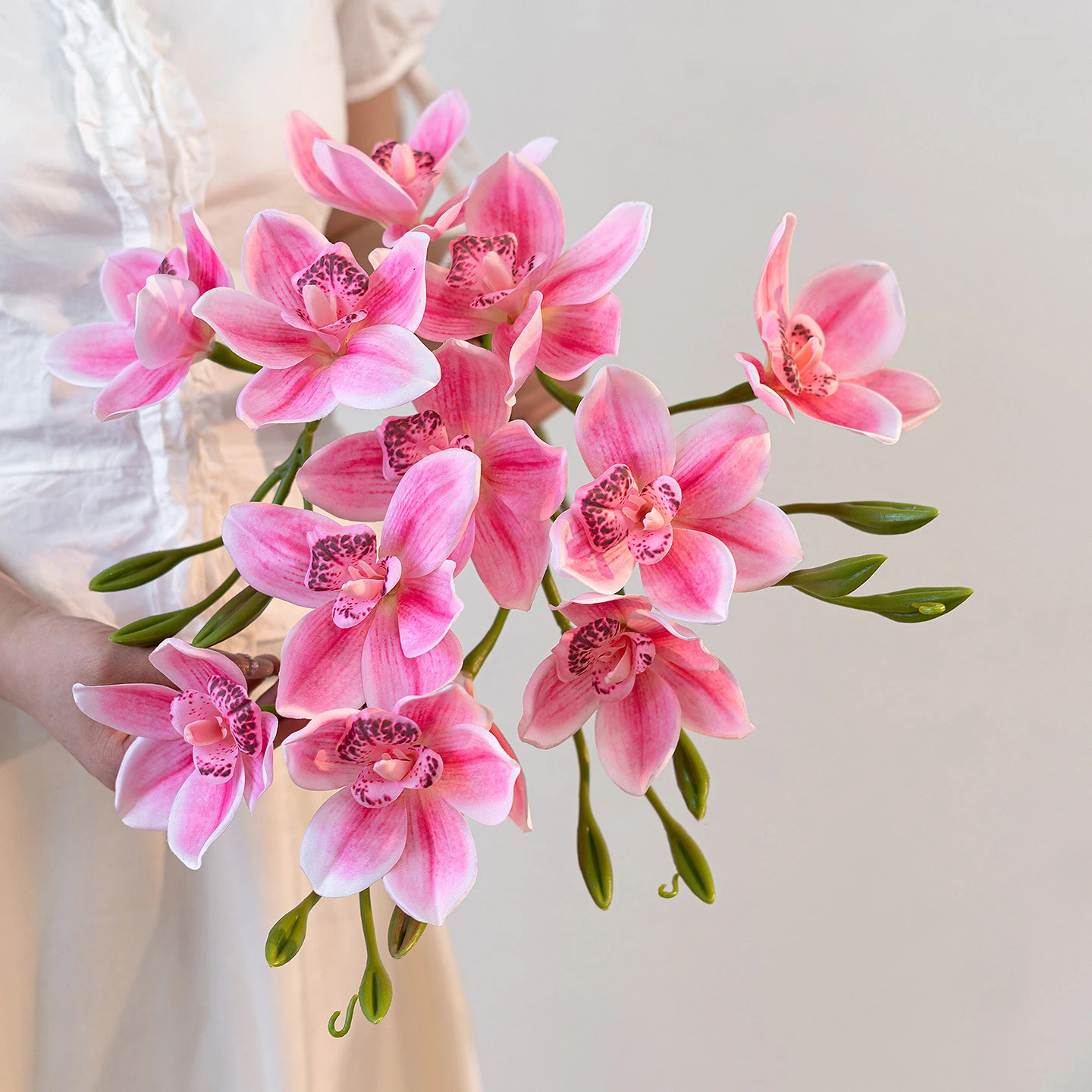 Artificial cymbidium orchid stem with several open blooms and buds along one arching cane with the full colour range