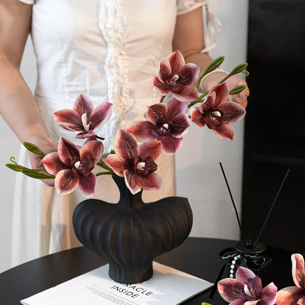 Artificial cymbidium orchid stem with several open blooms and buds along one arching cane, arranged in a vase