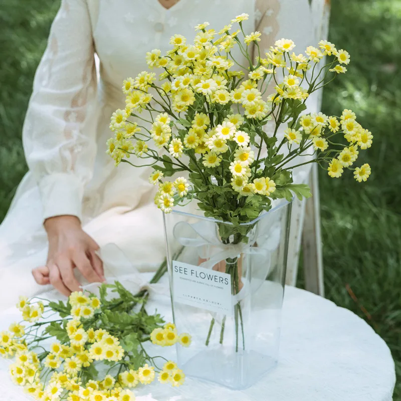 Yellow artificial daisy spray stem with open blooms, buds and feathery foliage, styled in a room setting