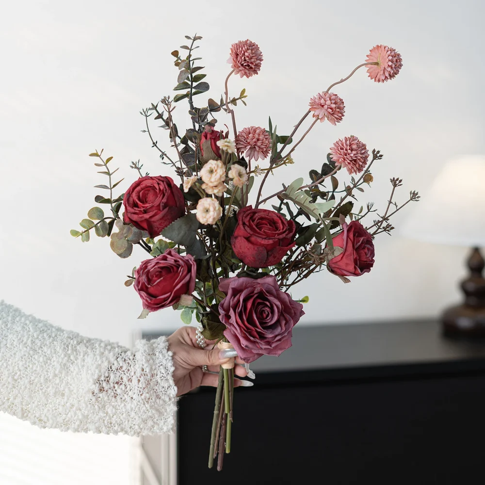 Burgundy artificial rose and eucalyptus bouquet built on a frame of eucalyptus stems, held in one hand
