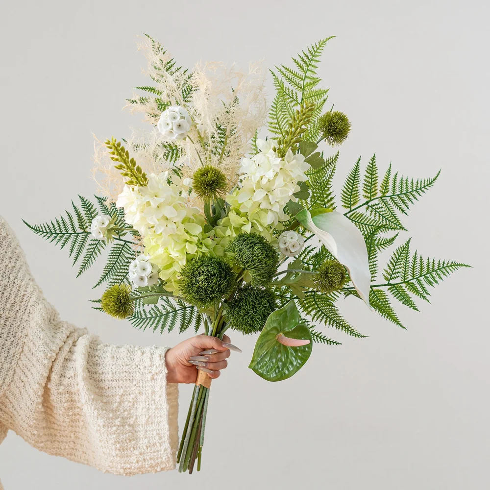 White and green artificial fern and flower bouquet built round a fan of fern fronds, held in one hand
