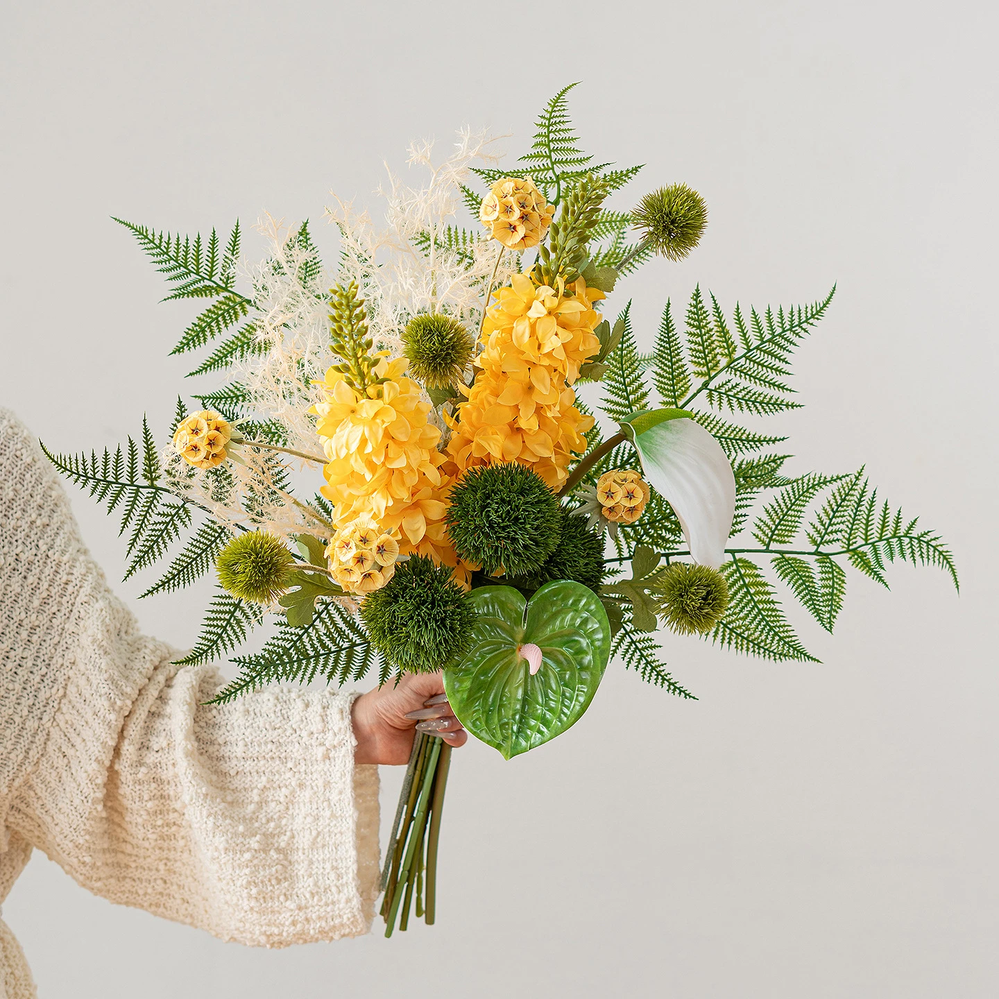 Yellow artificial fern and flower bouquet built round a fan of fern fronds, held in one hand