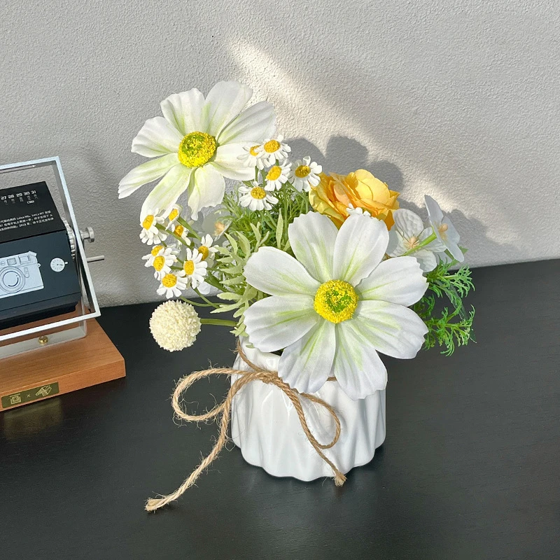 White and lemon artificial flower arrangement in a vase in a fluted white ceramic pot, styled on a table top