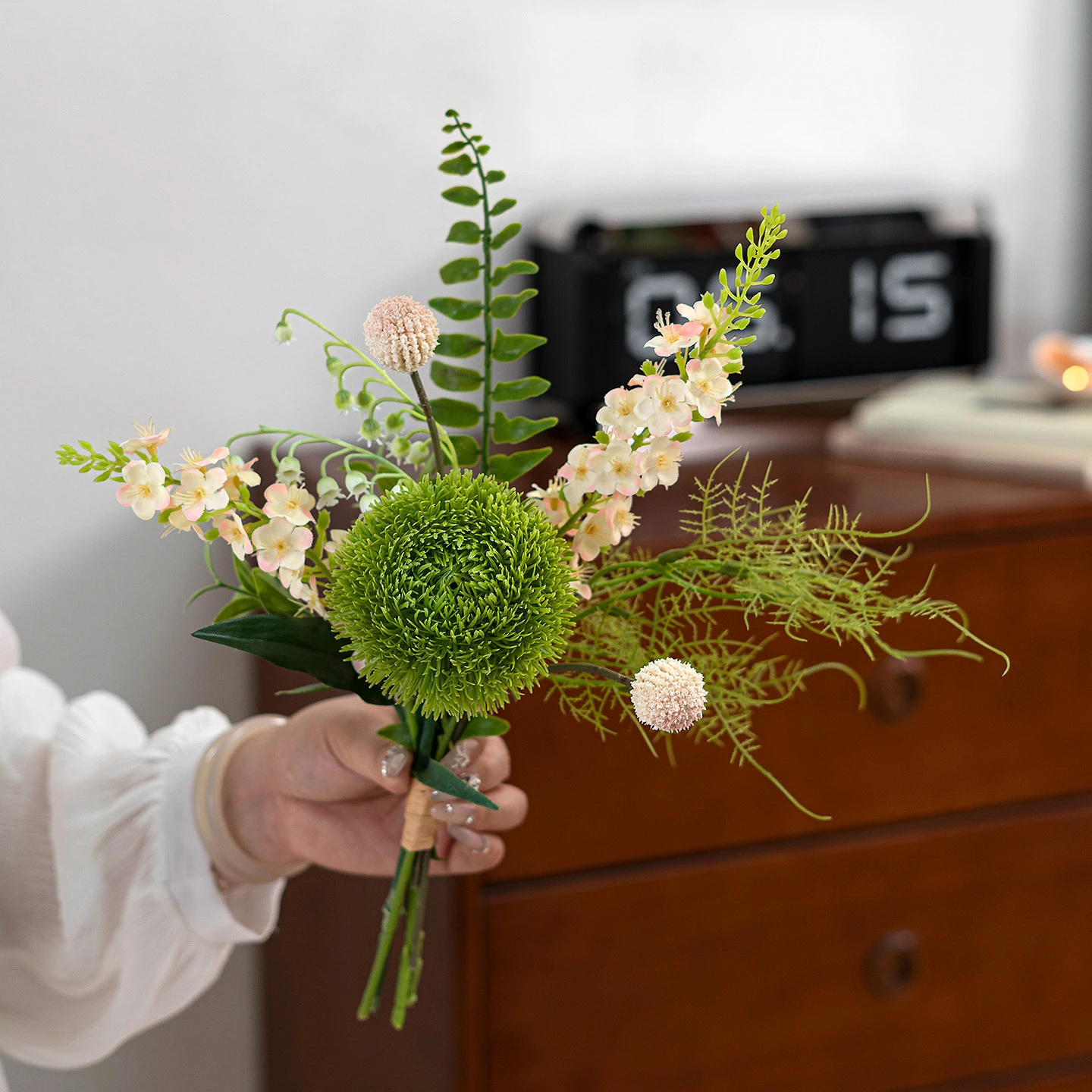 Cream artificial freesia and green dianthus posy built round one tight green dianthus head, held in one hand