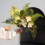 Lime artificial hand tied orchid bouquet with ferns and trailing Spanish moss, held in one hand