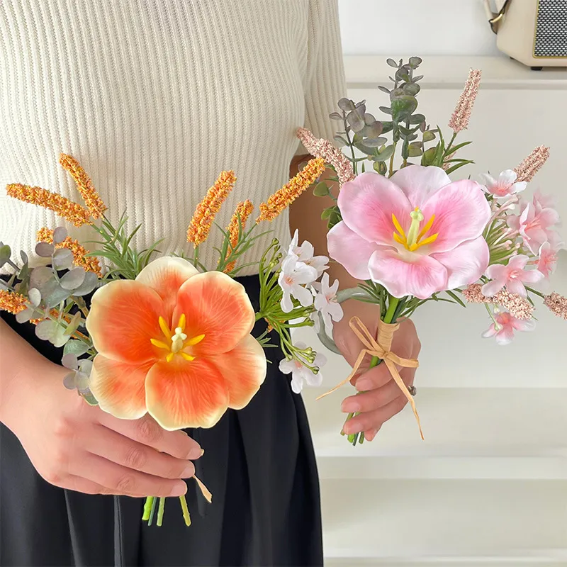 Coral and pink artificial hibiscus flower bunch tied with raffia round one large trumpet bloom, held in one hand