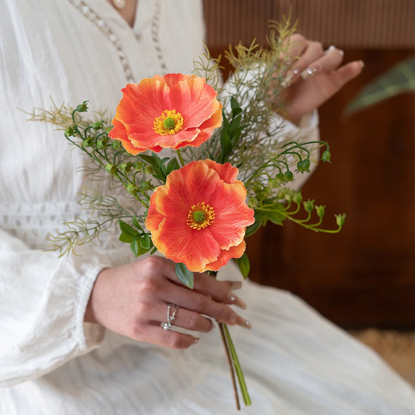 Orange artificial Iceland poppy stem with buds and fine fern foliage, styled in a room setting