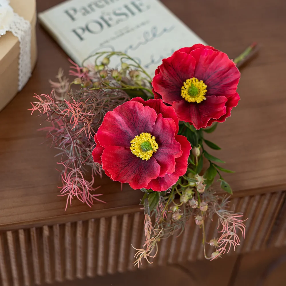 Red and wine artificial Iceland poppy stem with buds and fine fern foliage, styled on a table top