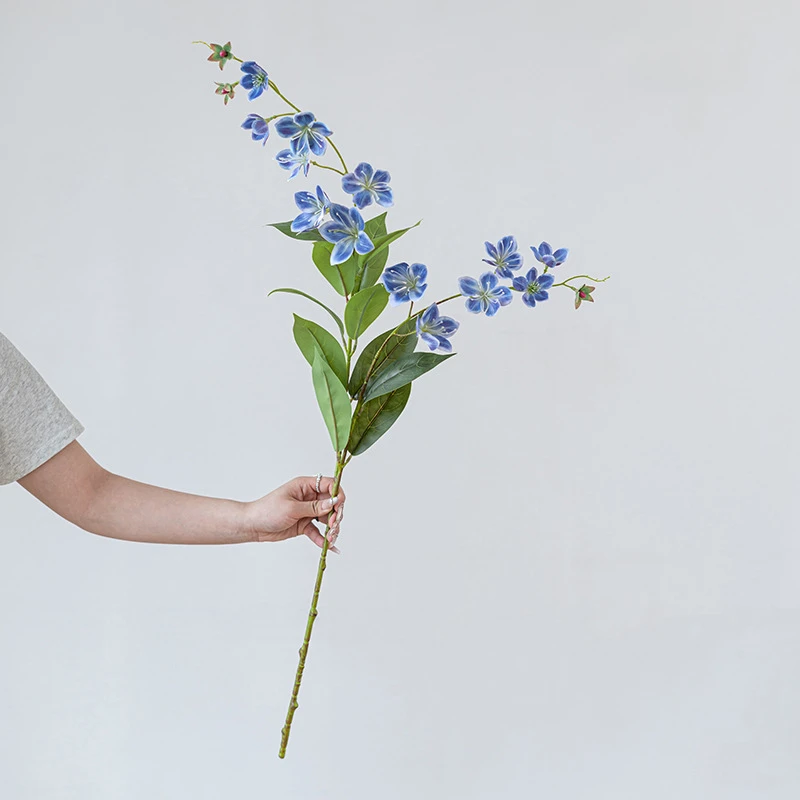 Blue long stem artificial flower spray with small five-petal blooms on a fine branching stem, held in one hand