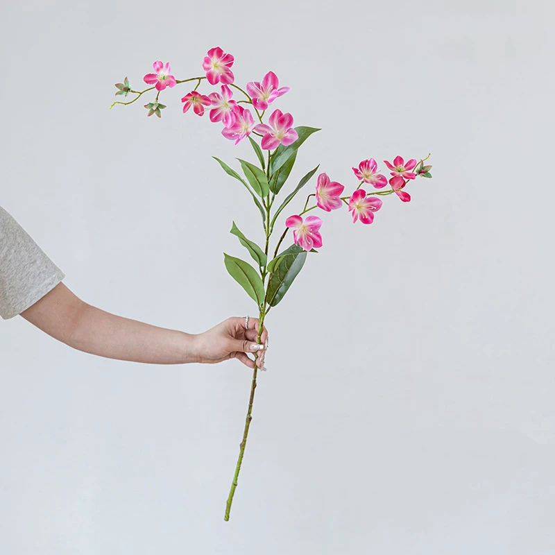 Cerise long stem artificial flower spray with small five-petal blooms on a fine branching stem, held in one hand