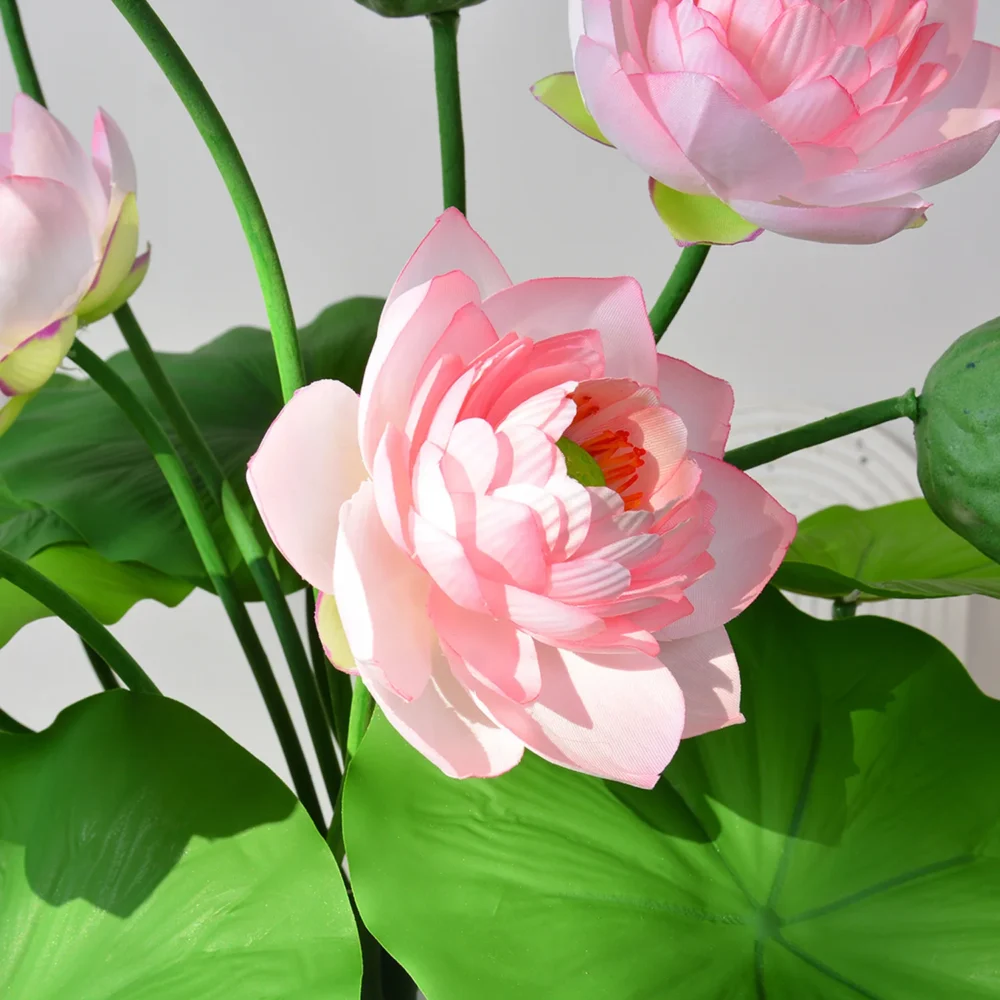 Pink artificial lotus flower arrangement with lotus pads, a seed head and buds shown close up