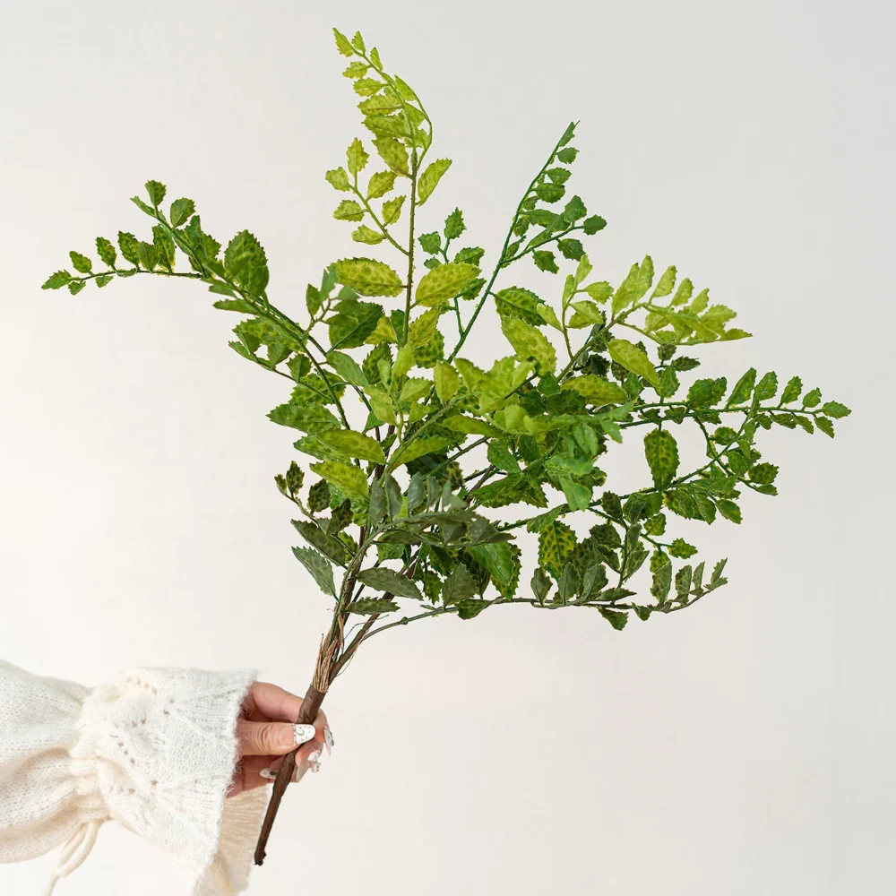 Bright green artificial maidenhair fern stem on fine black wire stems, held in one hand