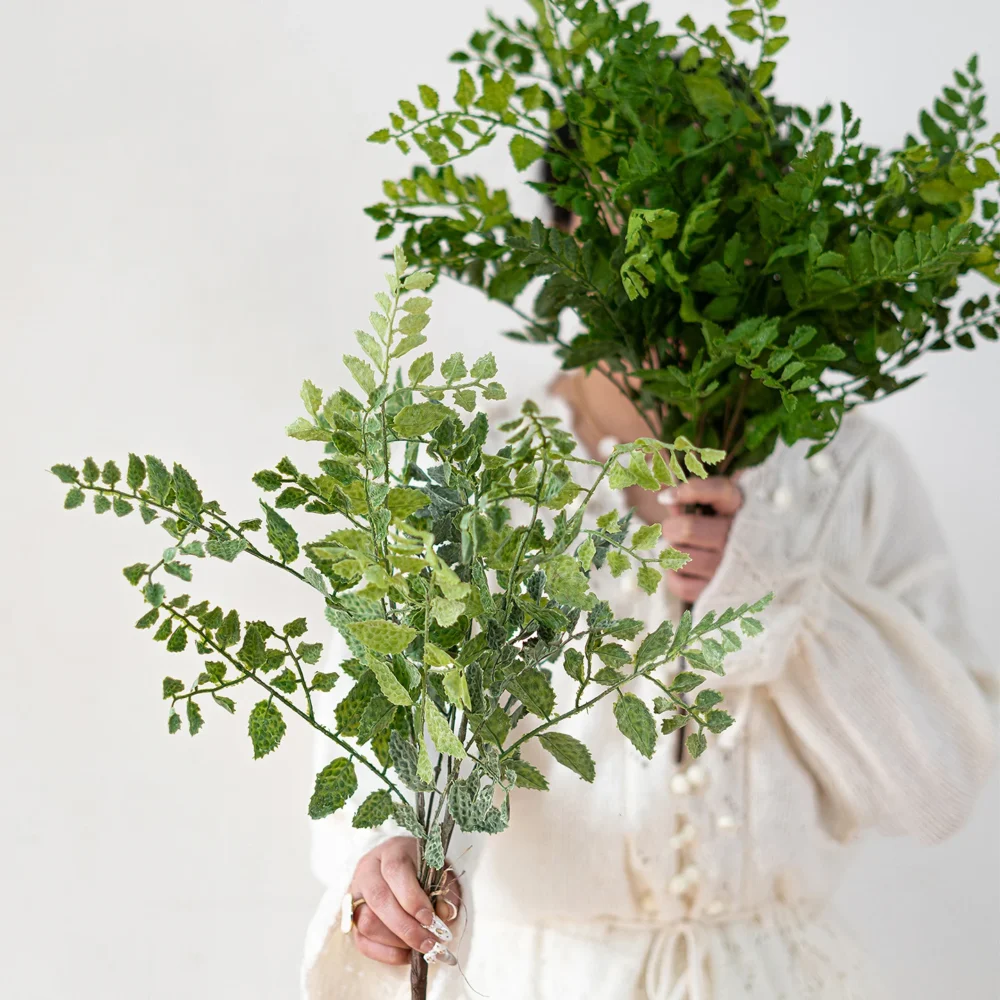 Deep green artificial maidenhair fern stem on fine black wire stems, held in one hand