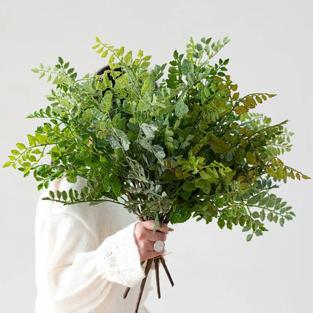 Mid green artificial maidenhair fern stem on fine black wire stems, held in one hand