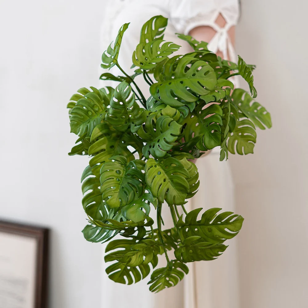 Tall stem artificial monstera leaf stem with split leaves twenty to thirty centimetres across, held in one hand