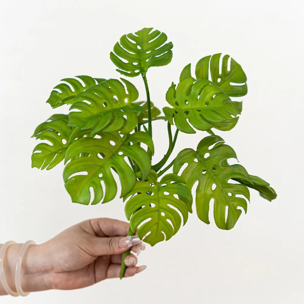 Twin leaf artificial monstera leaf stem with split leaves twenty to thirty centimetres across, held in one hand
