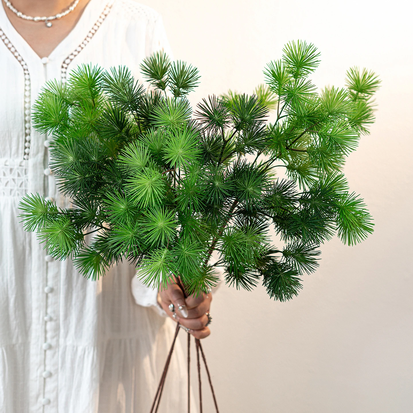 Dark green artificial pine branch with soft needled side shoots on a brown stem, held in one hand