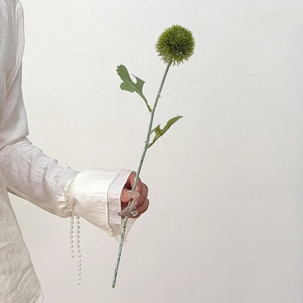 Green artificial pompom chrysanthemum stem with a dense spiky head, held in one hand