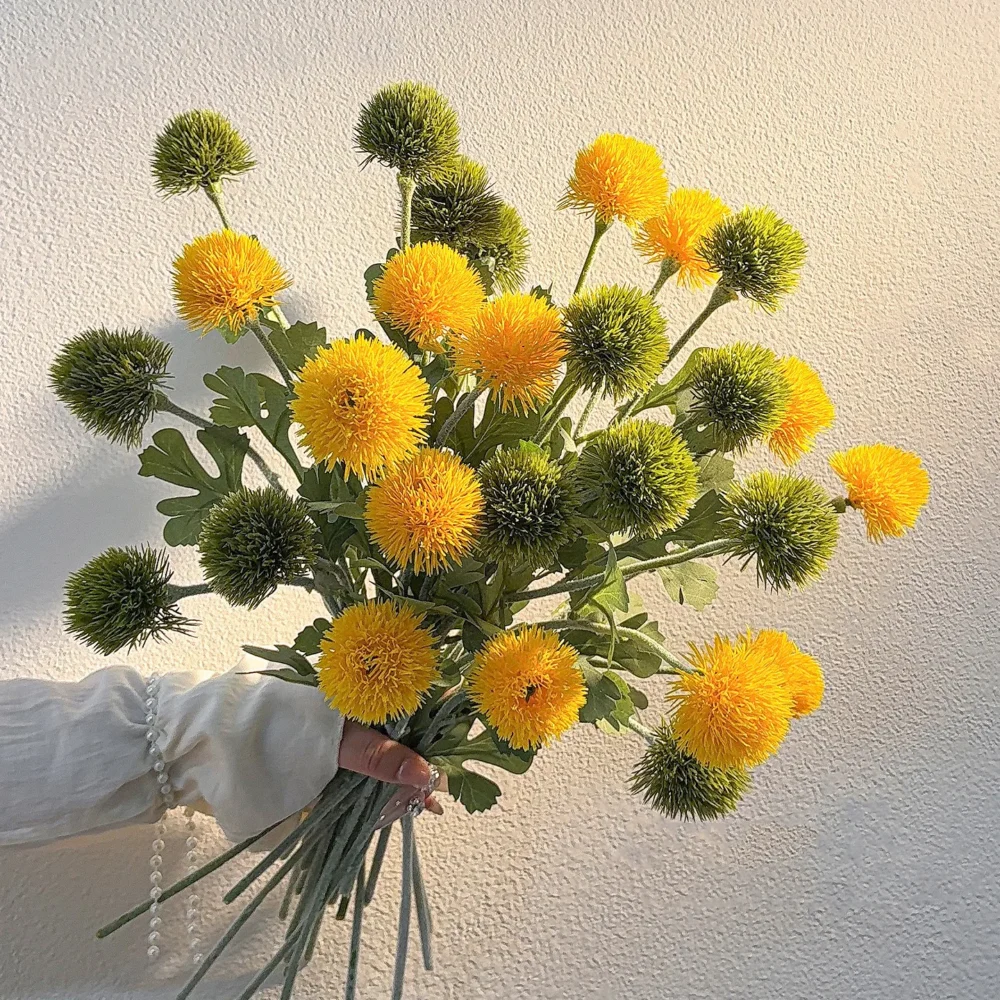 Artificial pompom chrysanthemum stem with a dense spiky head, held in one hand
