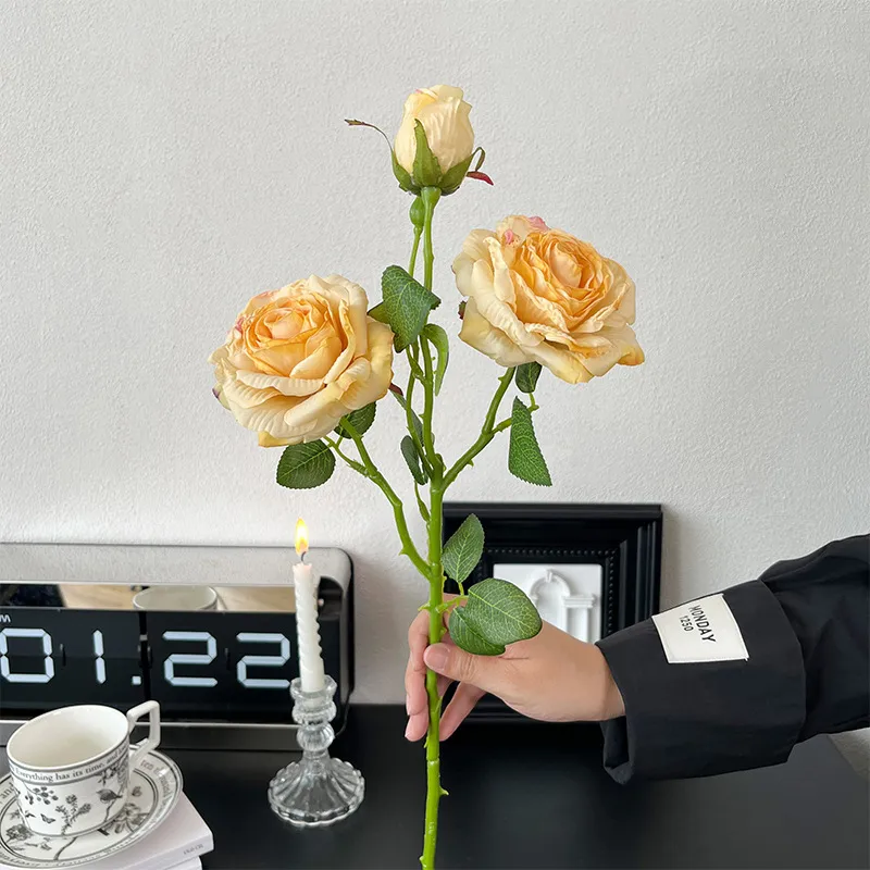 Apricot artificial rose spray stem with three heads at three stages of opening, held in one hand