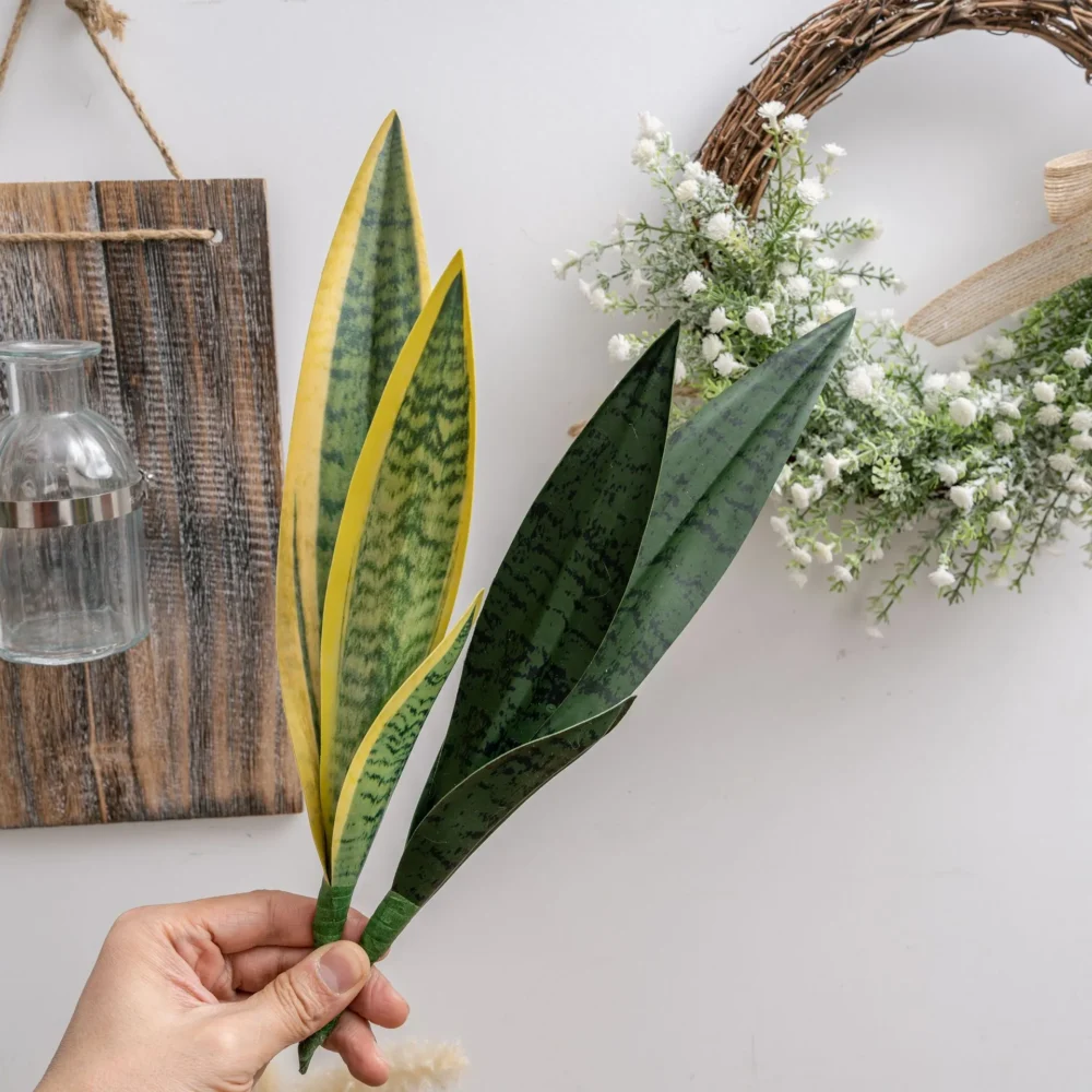 Artificial snake plant leaf with banded markings and a stiff blade, held in one hand