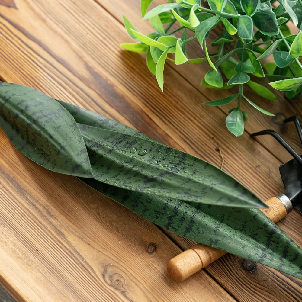 Artificial snake plant leaf with banded markings and a stiff blade, styled on a table top