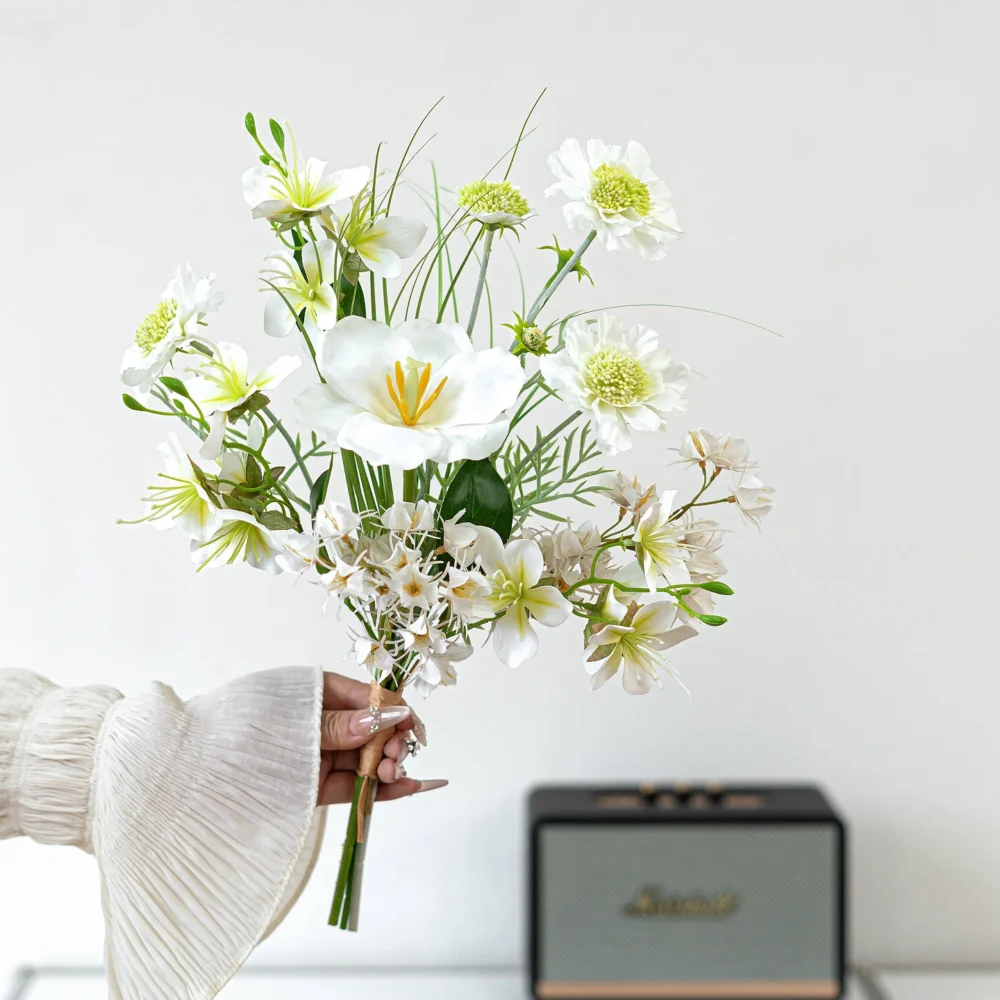 White and green artificial spring bouquet in blue and white of blue poppies, white blossom and fine grasses, held in one hand
