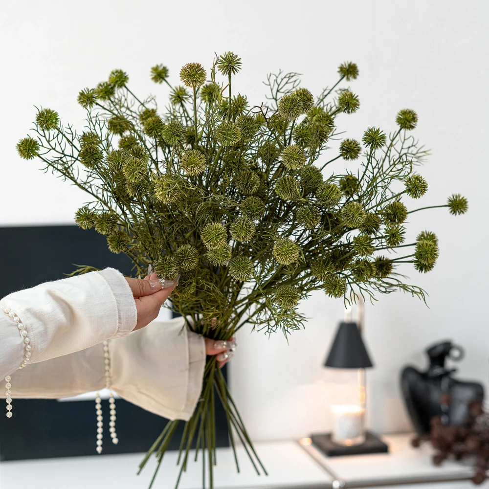 Green artificial thistle stem with spiked round seed heads on wiry branching stems, held in one hand
