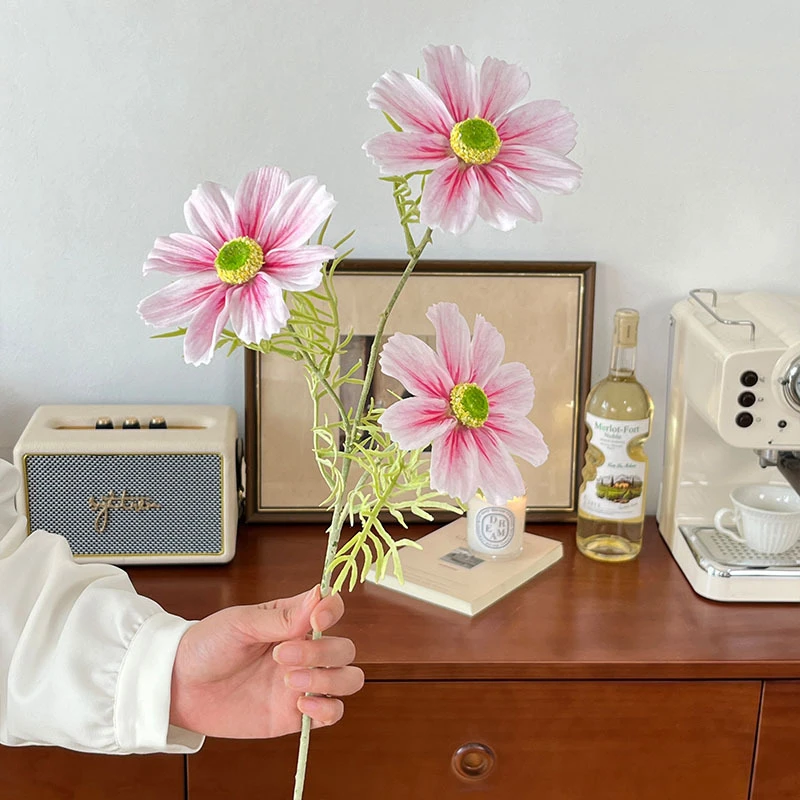 Pink big artificial cosmos stem with oversized open flower heads, held in one hand