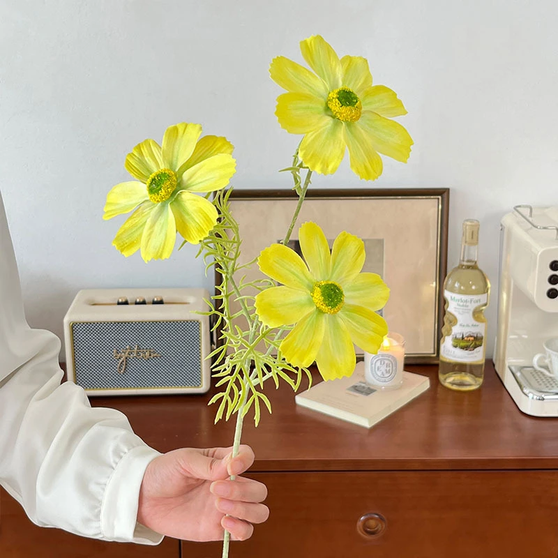 Yellow big artificial cosmos stem with oversized open flower heads, held in one hand