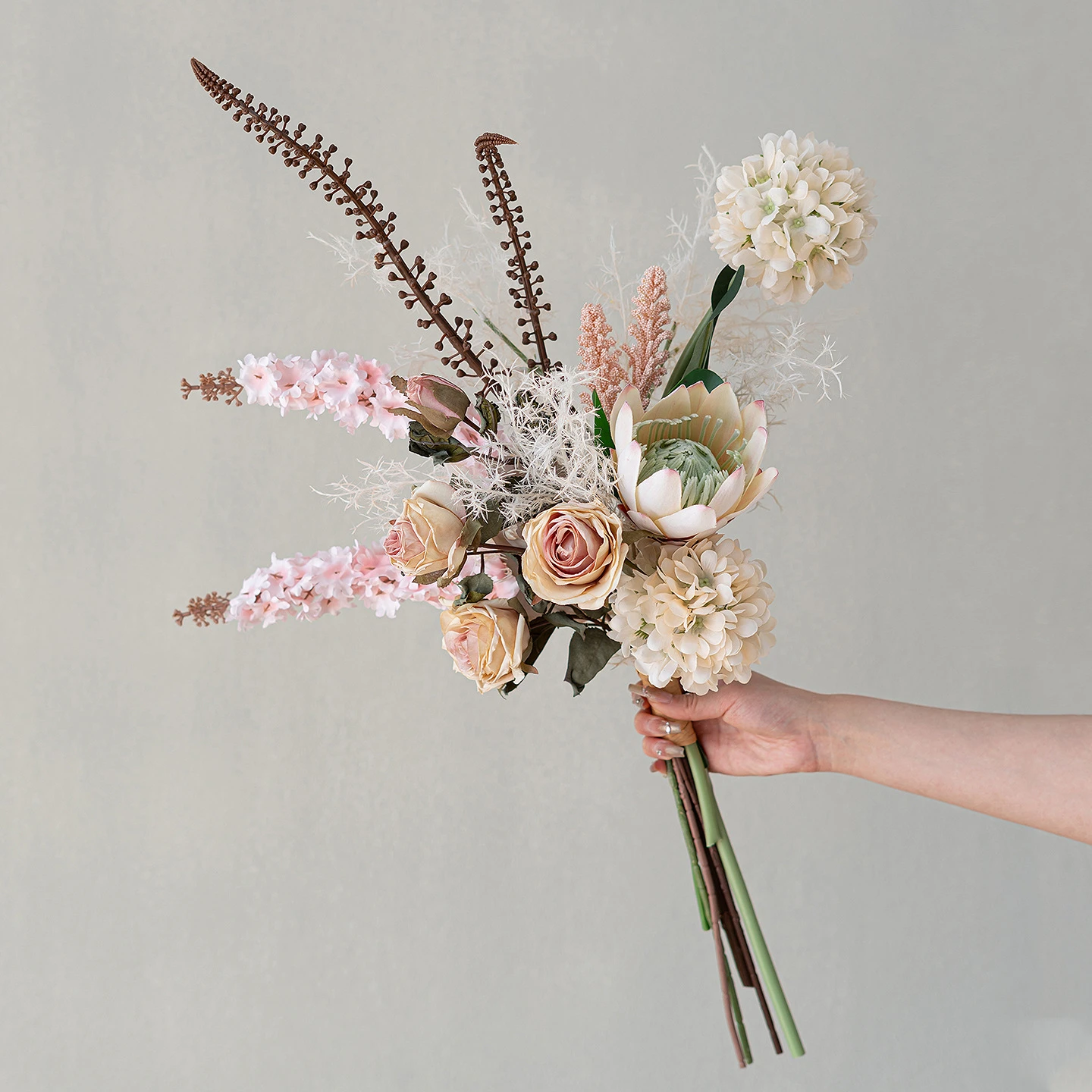 Pale pink artificial boho wedding bouquet in rust and terracotta with pampas and palm fans, held in one hand