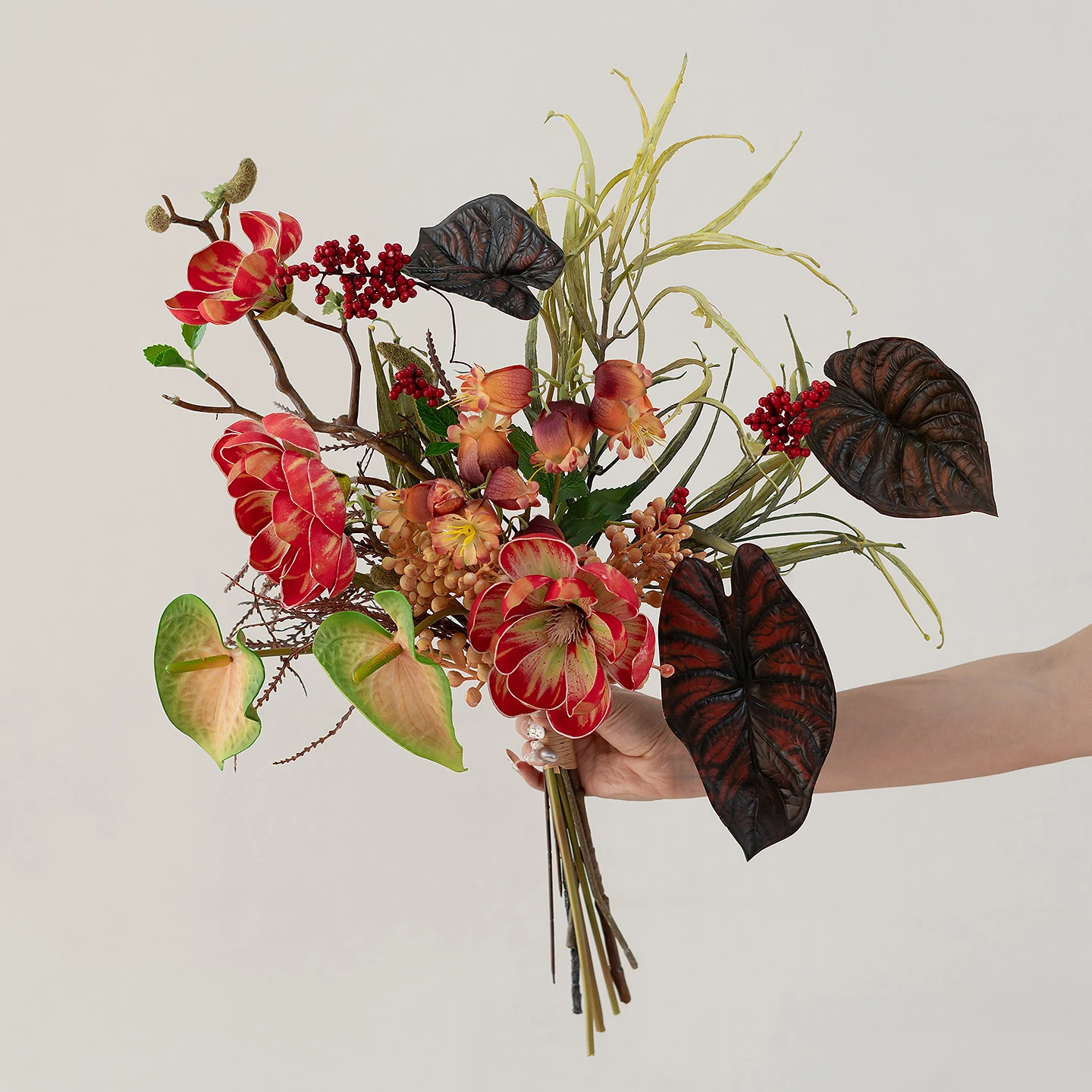 Red and green artificial boho wedding bouquet in rust and terracotta with pampas and palm fans, held in one hand