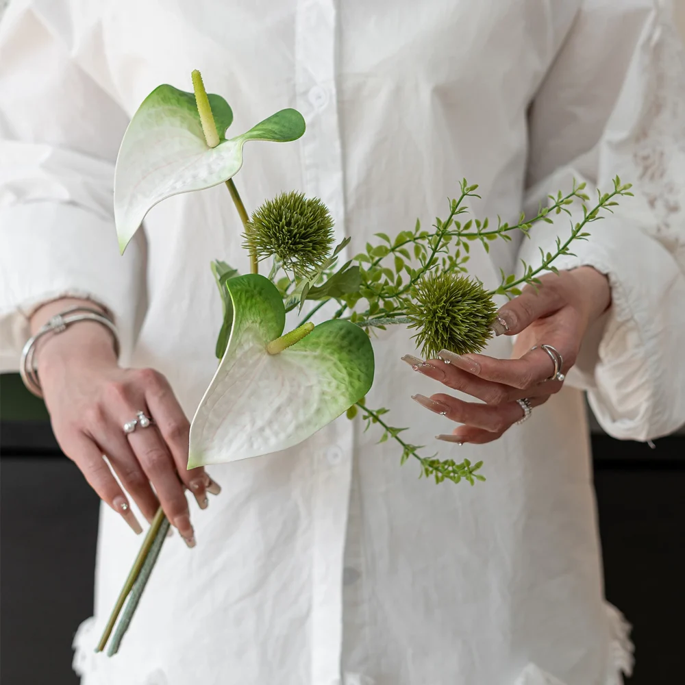 Lime artificial bud vase arrangement of two anthurium and one spiked green stem, held in one hand