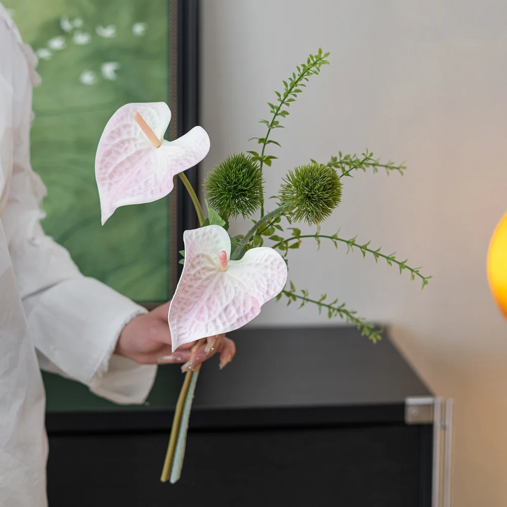 Pale pink artificial bud vase arrangement of two anthurium and one spiked green stem, held in one hand