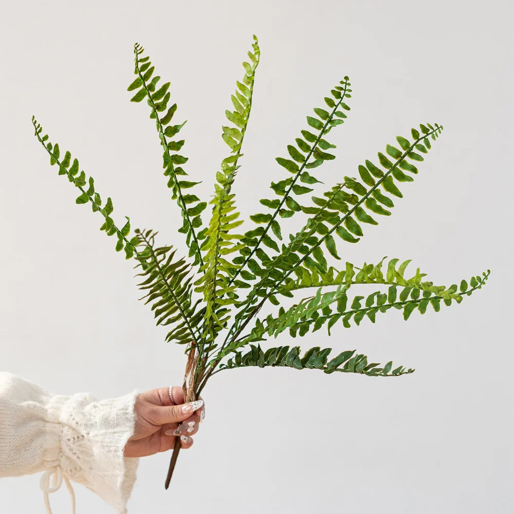 Bright green large artificial fern frond, sixty centimetres from base to tip, held in one hand