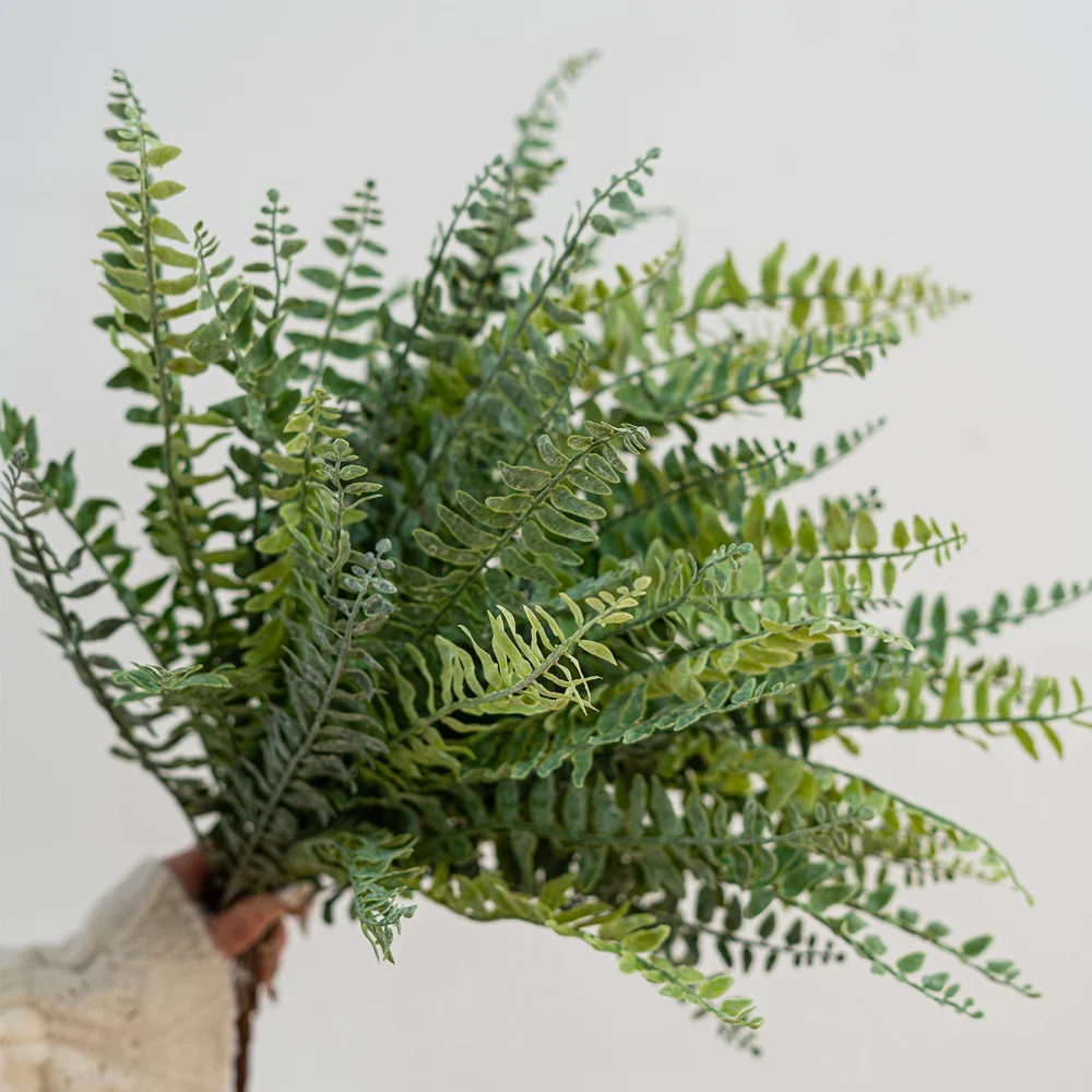 Green large artificial fern frond, sixty centimetres from base to tip, held in one hand