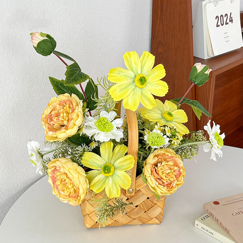 Yellow artificial flower basket arrangement in a woven basket with an upright handle, styled on a table top