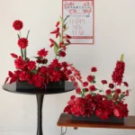 Red artificial flower table arrangement in a low black base, styled in a room setting