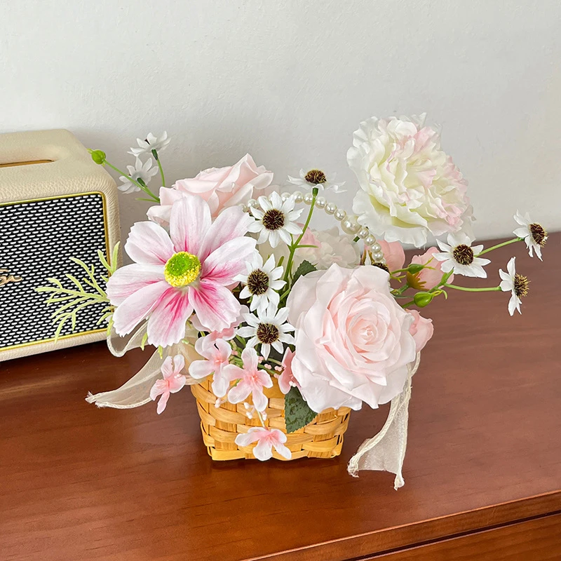 Pink rose small artificial flower gift basket tied with a wide organza bow, styled on a table top