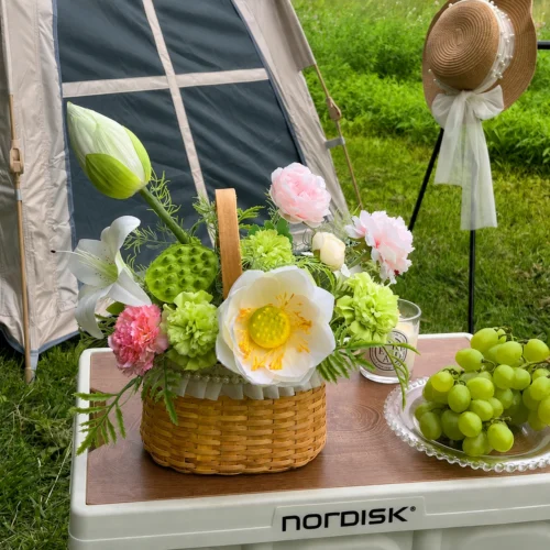 White and lime artificial summer flower basket in a round cane basket with an upright handle, styled in a room setting