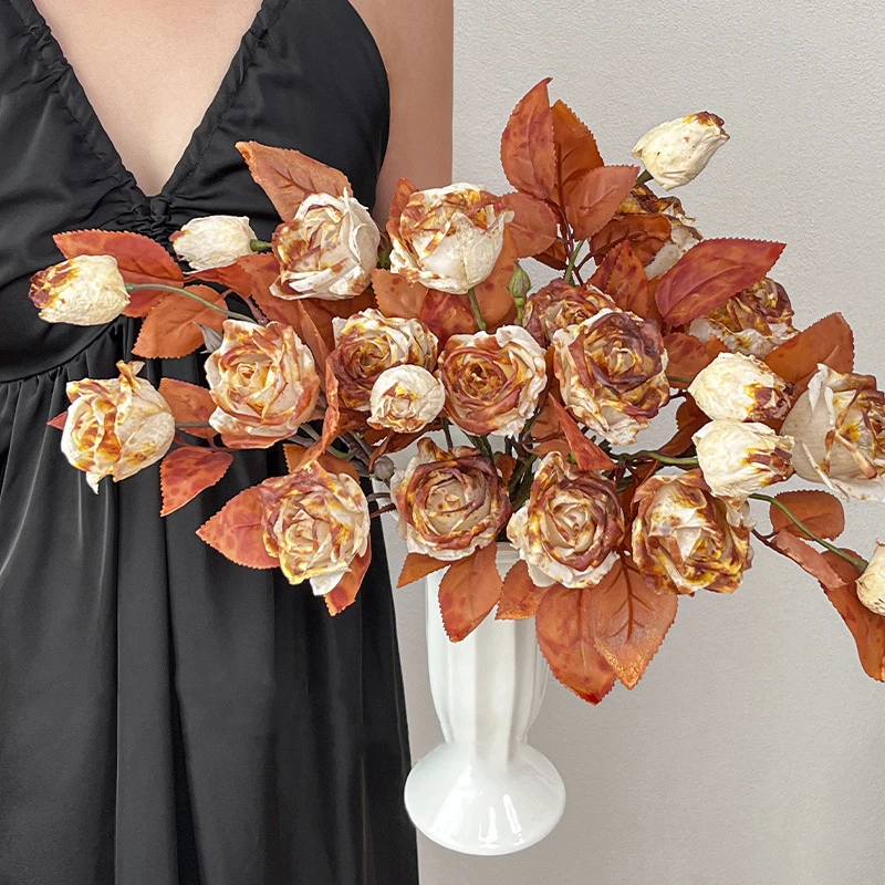 Vintage artificial rose stem with three dried-look heads and rust foliage, styled in a room setting