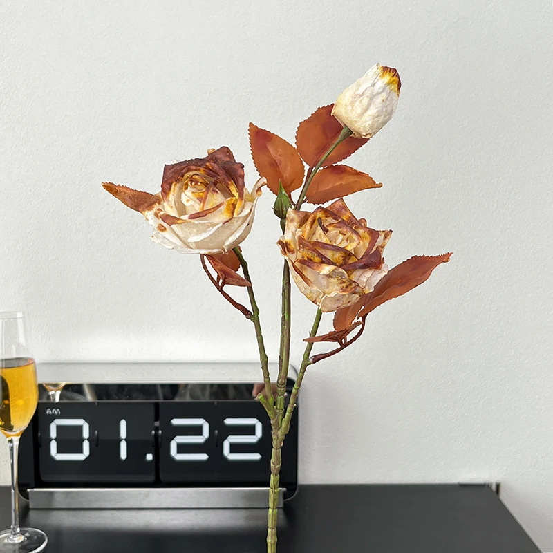 Sand vintage artificial rose stem with three dried-look heads and rust foliage, styled on a table top