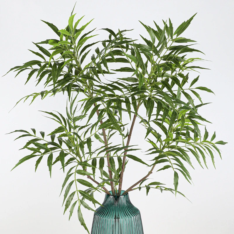 In a green vase artificial bamboo stem with narrow leaves layered along a jointed cane, arranged in a vase