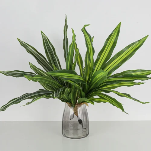 In a glass vase artificial dracaena leaf cluster with aerial roots left on so it plants straight into a pot, arranged in a vase
