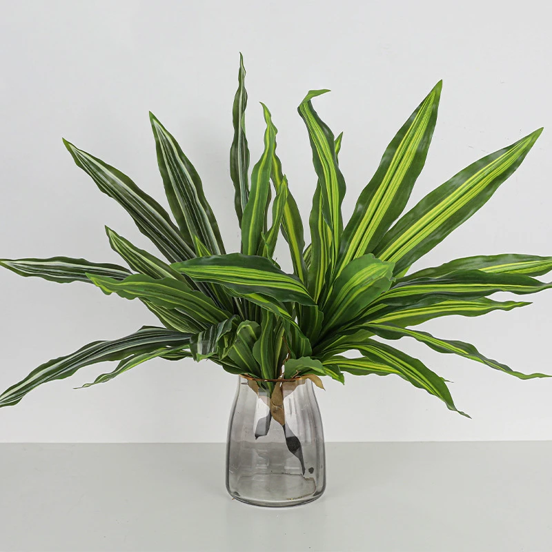 In a glass vase artificial dracaena leaf cluster with aerial roots left on so it plants straight into a pot, arranged in a vase