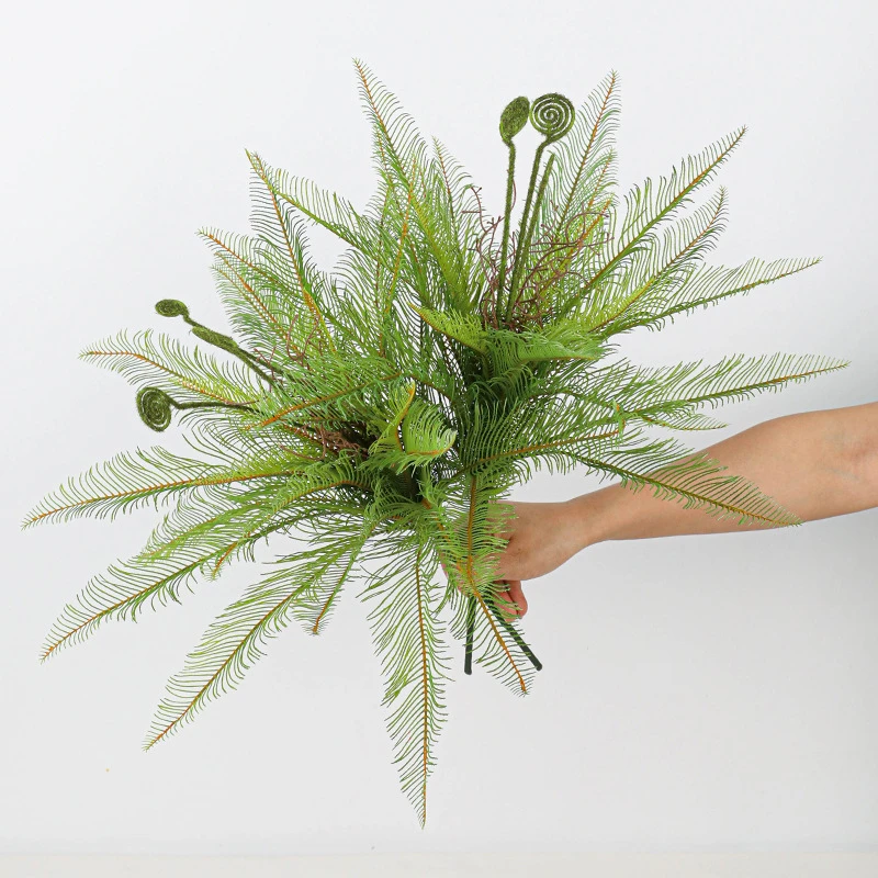 Wide bush artificial fern bush with coiled fiddleheads left unopened among the fronds, held in one hand